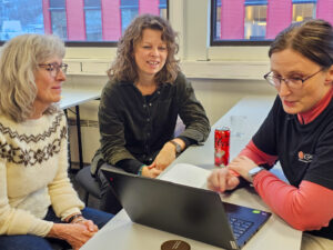 Bilde av tre damer som sitter rundt et bord og ser på en datamaskin