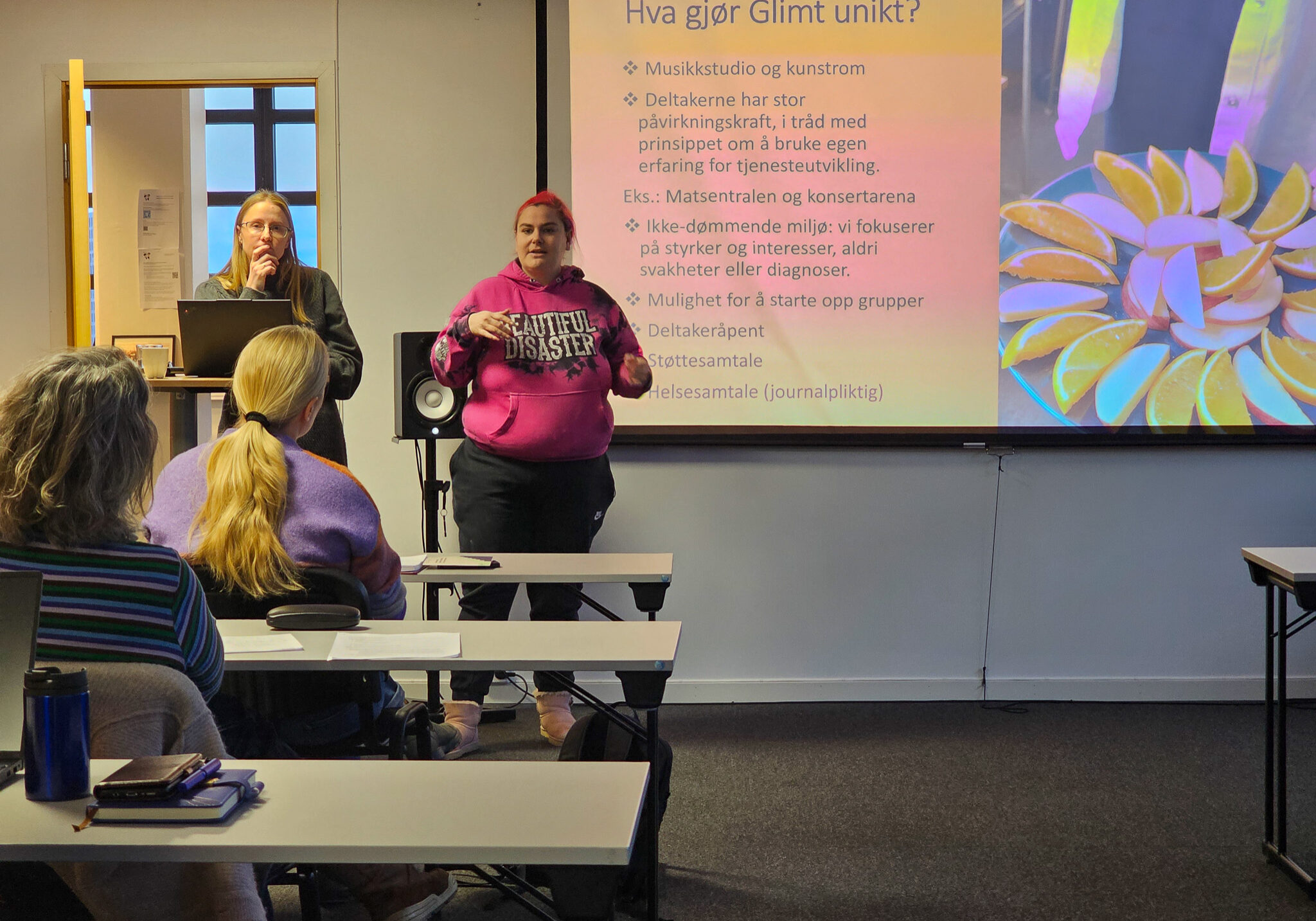 Bilde fra et klasserom, hvor to damer står og hoder foredrag for flere tilskuere