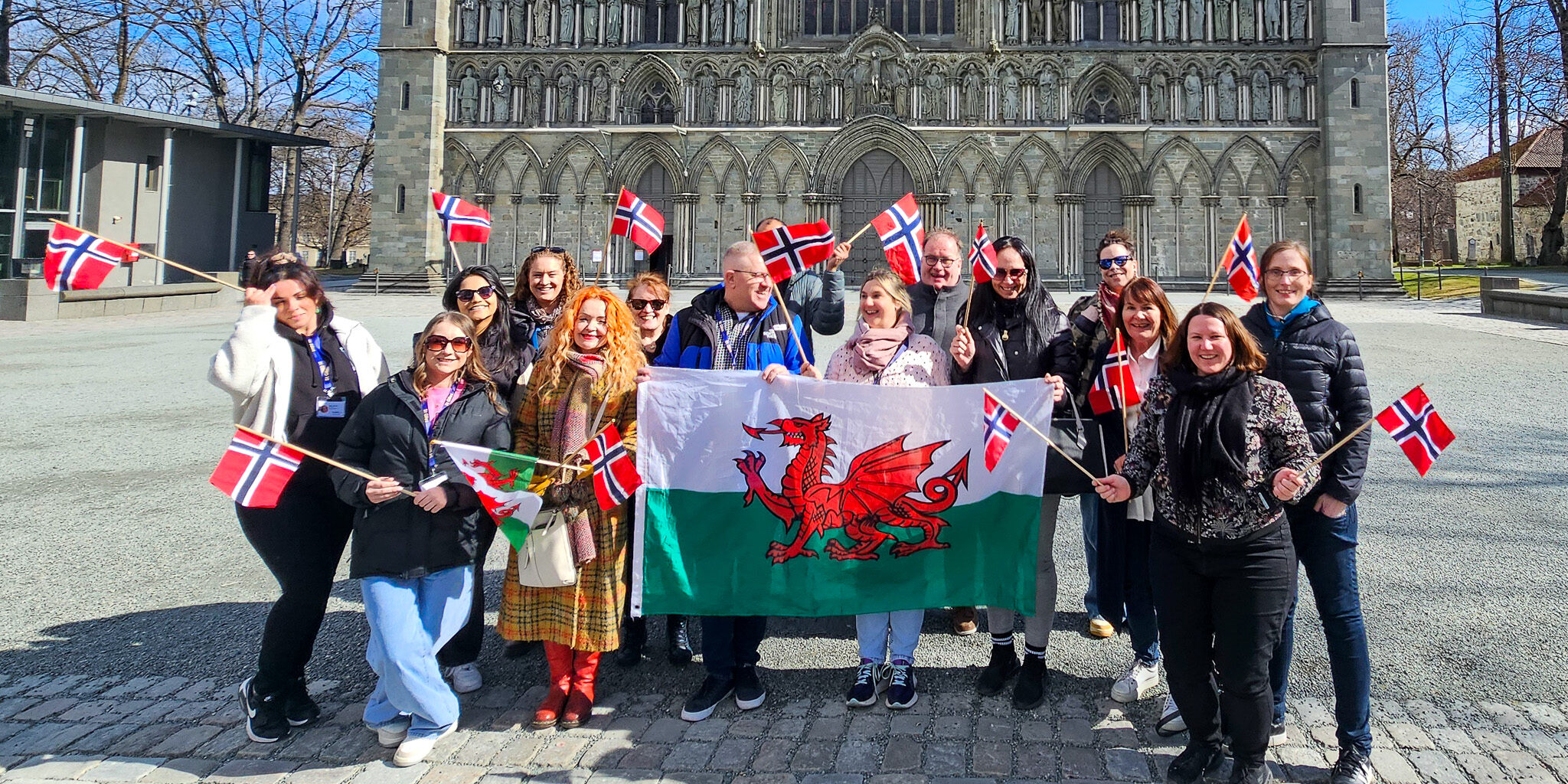 Bilde av en gruppe mennesker foran Nidarosdomen. Gruppen holder opp flagg fra Wales og Norge.